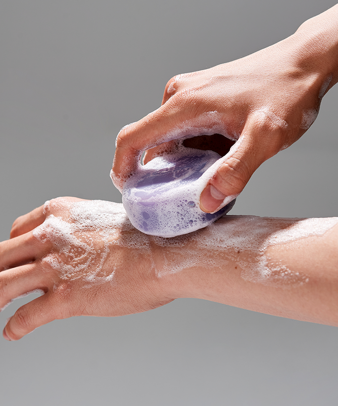 Person using DONGGUBAT Field Correct Cleansing Soap Collagen on arm, producing a lather with purple soap.