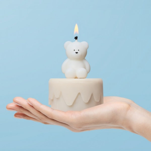 Hand holding a cute bear-shaped candle on a small round base against a light blue background.