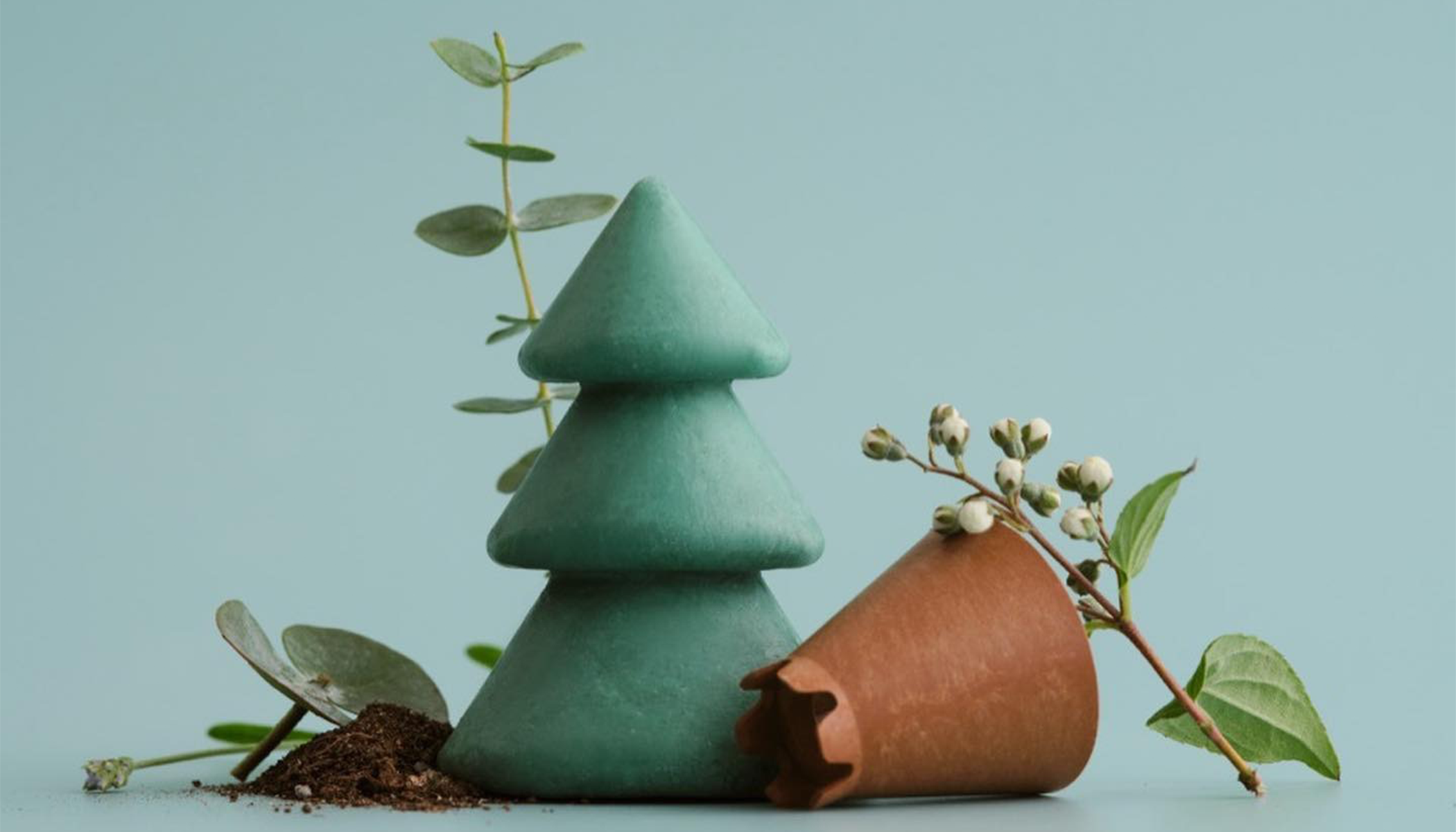 Green cone-shaped candles with eucalyptus leaves and clay pot on light background