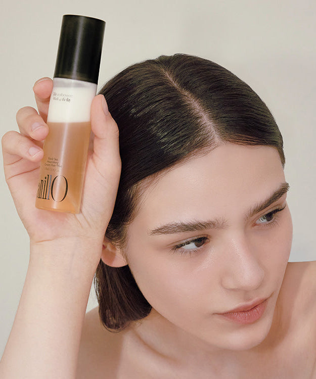 Model holding ANILLO Black Tea Nourishing Cream Hair Mist 70ml bottle near face