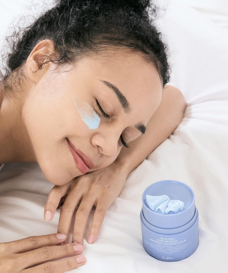 Woman applying DR.ALTHEA Pore Refresh Grinding Cleansing Balm 50ml on face while relaxing on bed