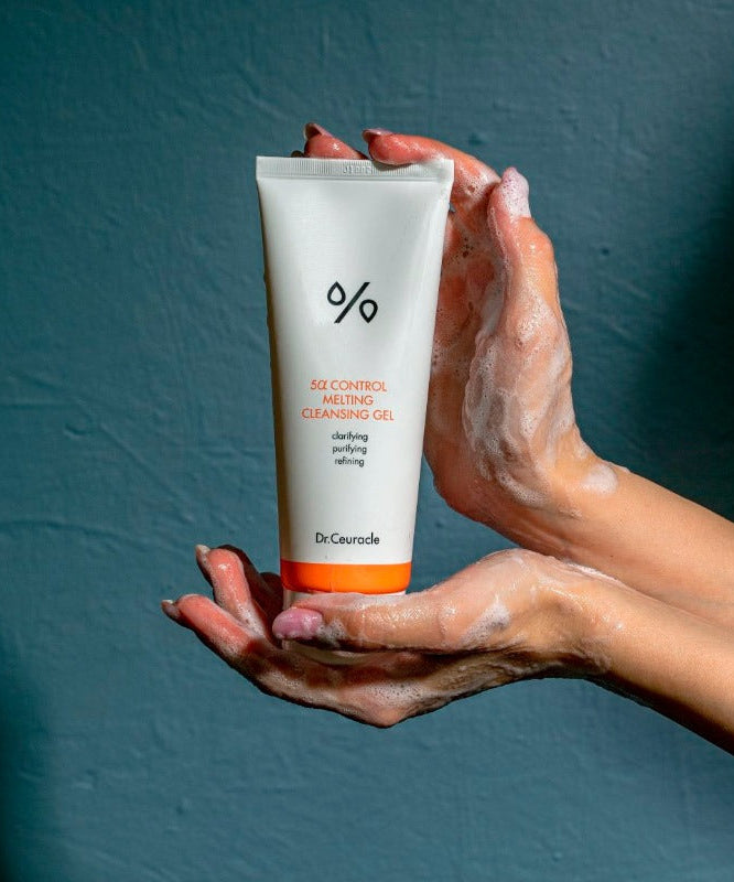 Hands holding DR.CEURACLE 5 Alpha Control Melting Cleansing Gel 150ml against a dark background.