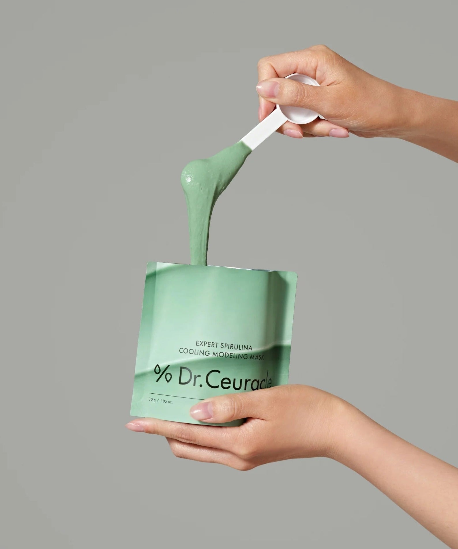 Person applying DR.CEURACLE Expert Spirulina Cooling Modeling Mask 30g with a spatula, showcasing smooth texture and packaging.