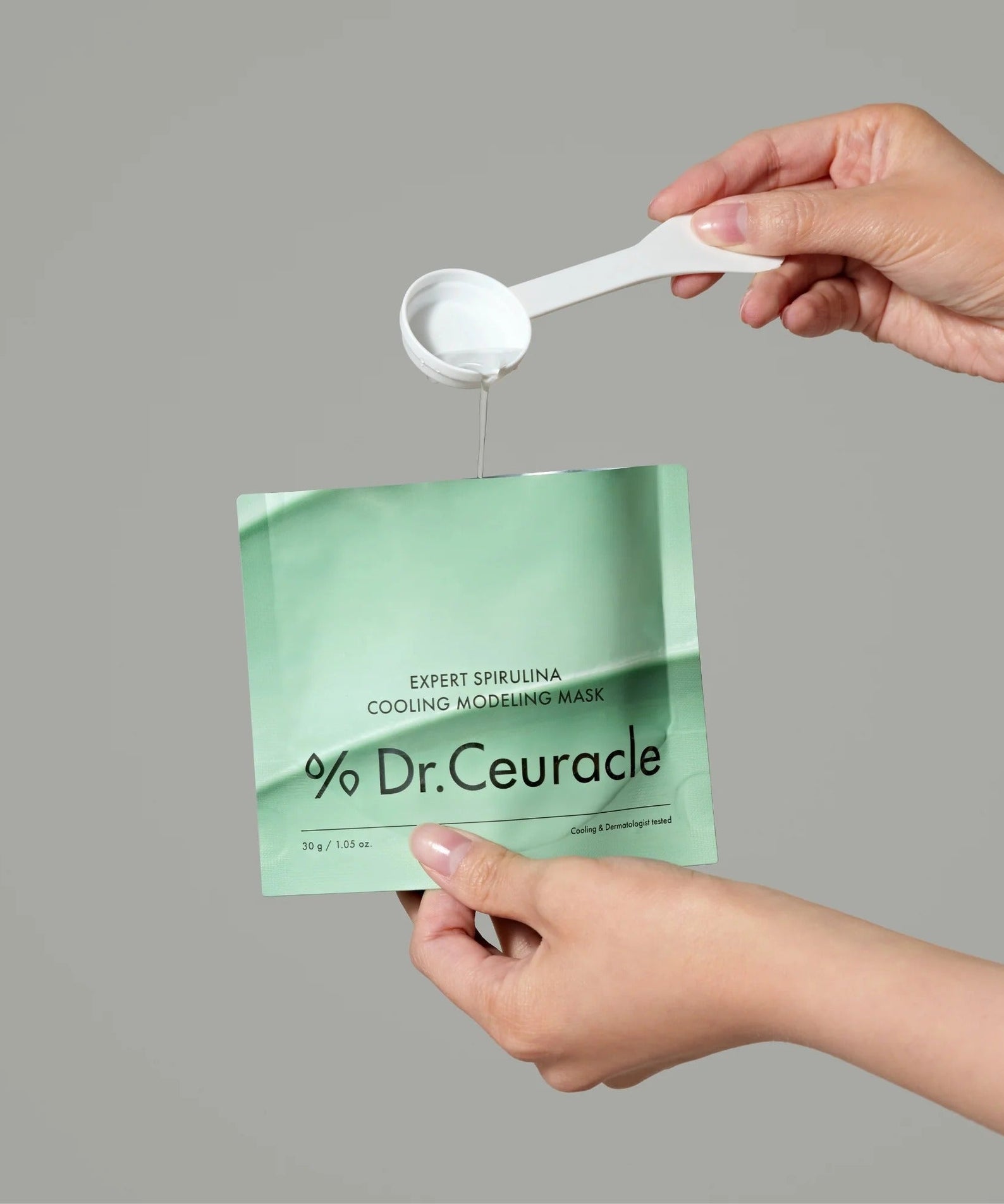 Hands holding DR.CEURACLE Expert Spirulina Cooling Modeling Mask 30g with spoon.