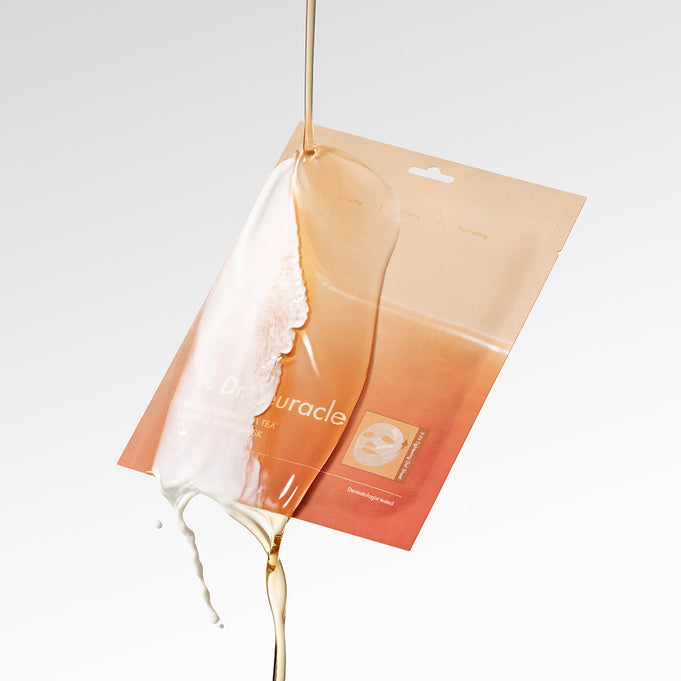 An open package of DR.CEURACLE Vegan Kombucha Tea Essence-in-Gel Mask with essence dramatically pouring over it on a white background.