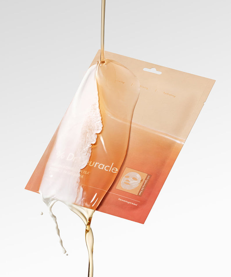 An open package of DR.CEURACLE Vegan Kombucha Tea Essence-in-Gel Mask with essence dramatically pouring over it on a white background.