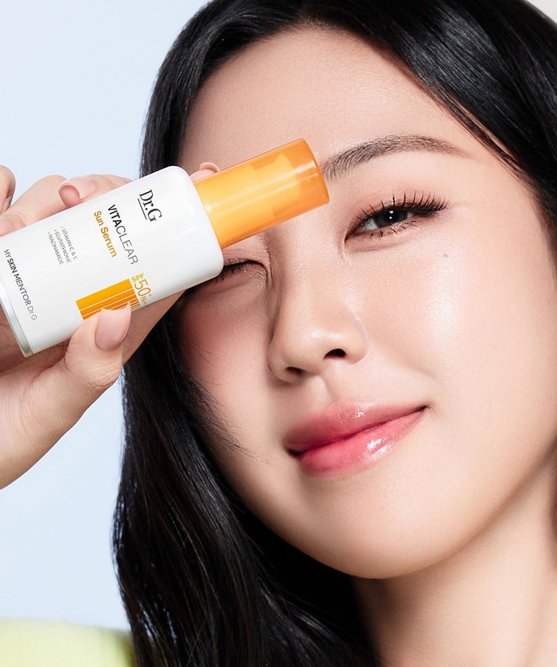 Woman holding DR.G Vita Clear Sun Serum 50ml next to her face showing skincare product application.