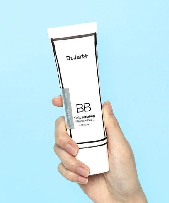 Hand holding DR.JART+ BB Rejuvenating 50ml tube against blue background