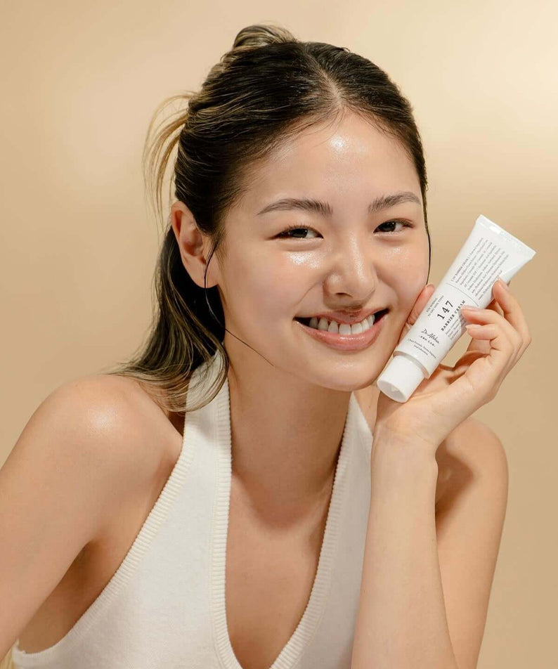 Smiling person holding DR.ALTHEA 147 Barrier Cream 50ml, showcasing skincare product.