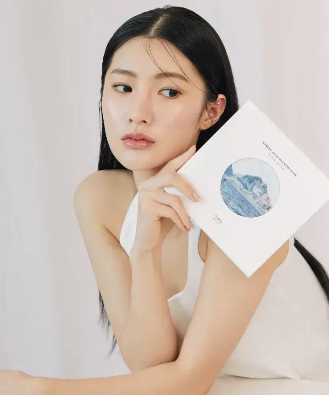 Woman holding DR.ALTHEA Marine Anti Blemish Mask (5ea) in hand wearing a white top with a neutral expression.