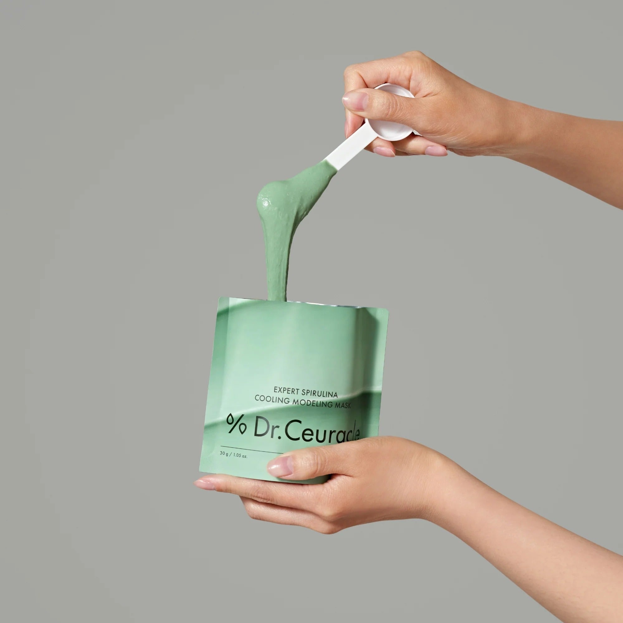 Person applying DR.CEURACLE Expert Spirulina Cooling Modeling Mask 30g with a spatula, showcasing smooth texture and packaging.