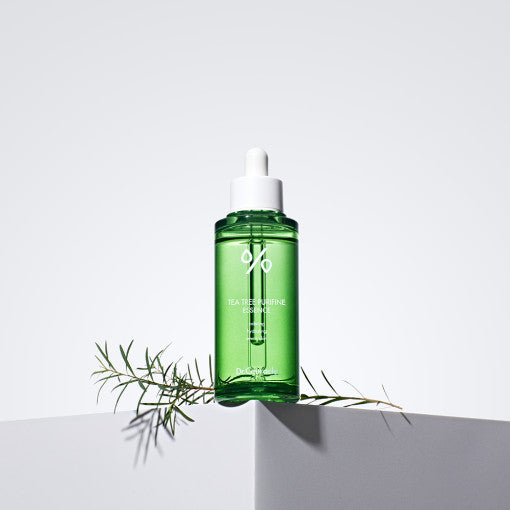 Green bottle of DR.CEURACLE Tea Tree Purifine Essence 50ml with white dropper on a white background with tea tree leaves.