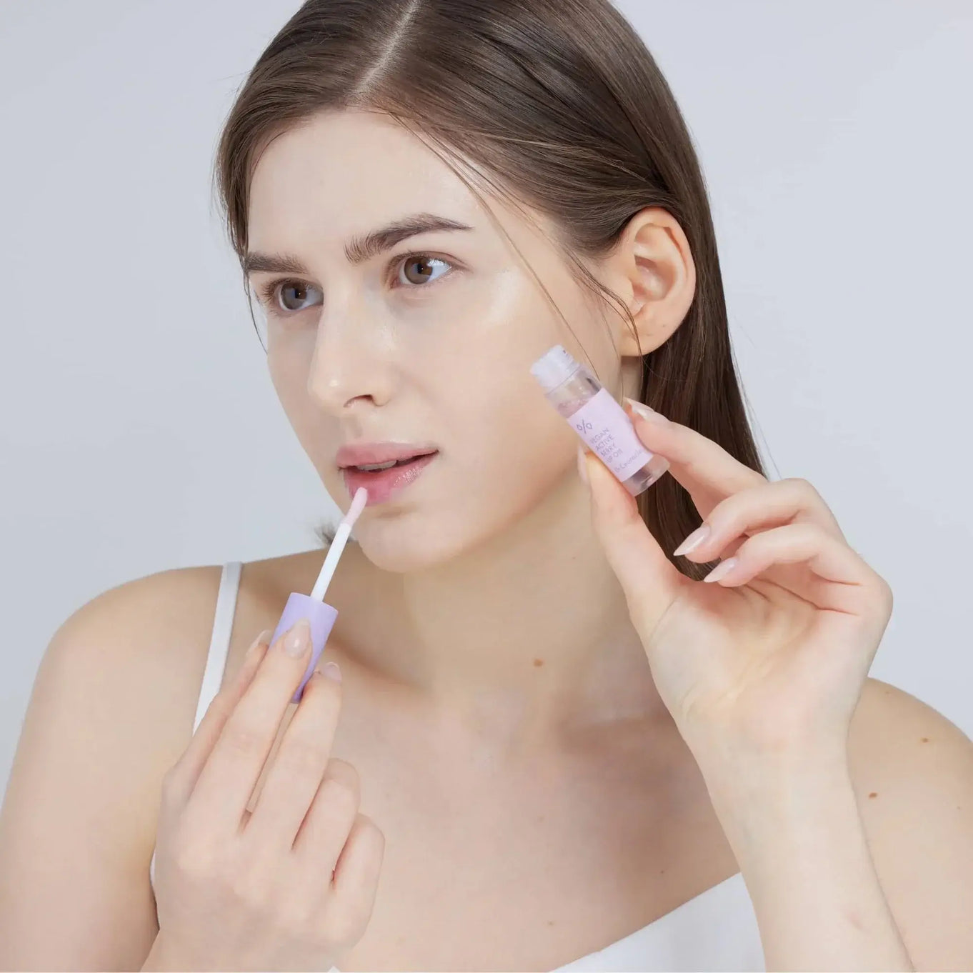 Woman applying DR.CEURACLE Vegan Active Berry Lip Oil for moisturizing lips.