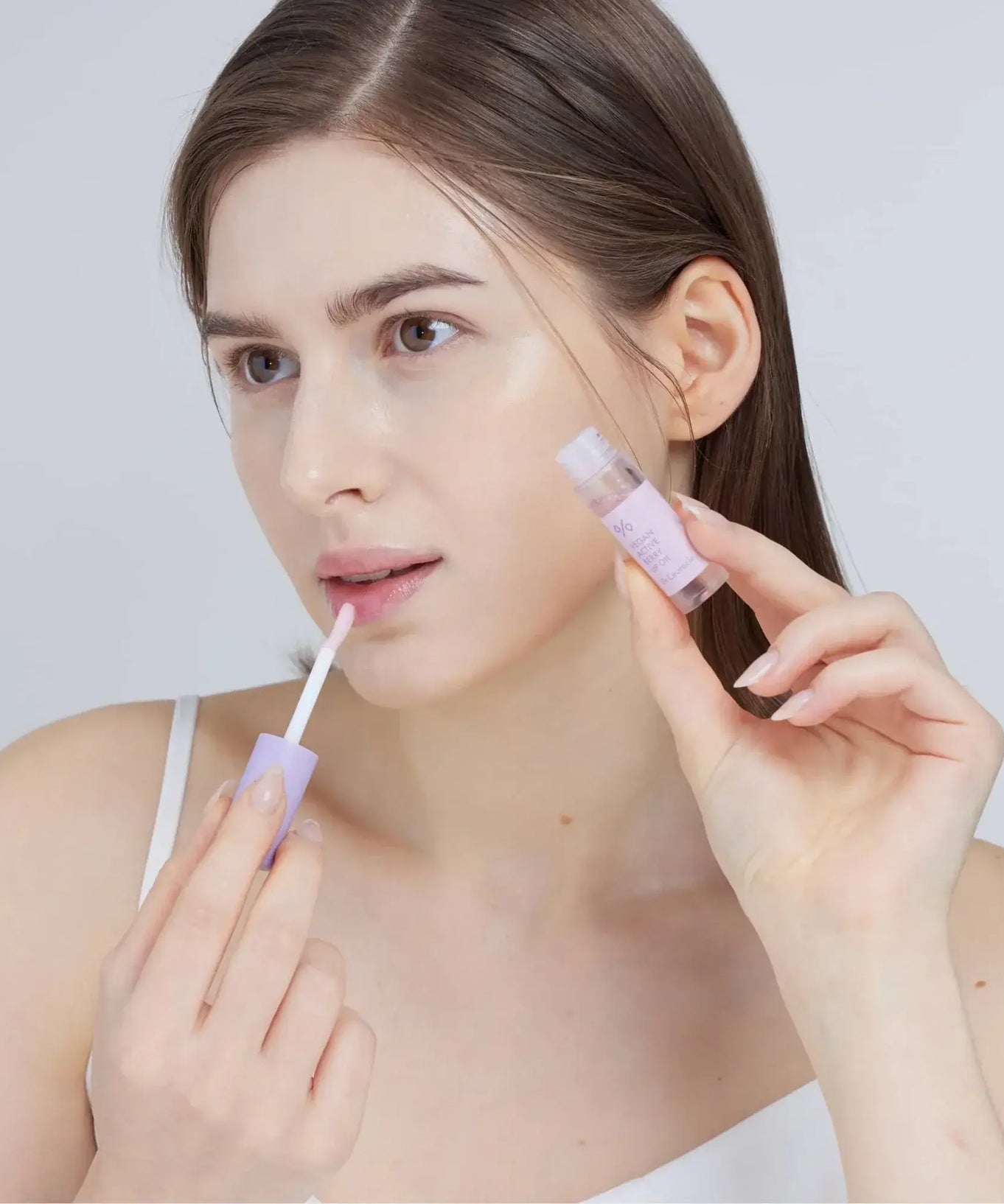 Woman applying DR.CEURACLE Vegan Active Berry Lip Oil for moisturizing lips.
