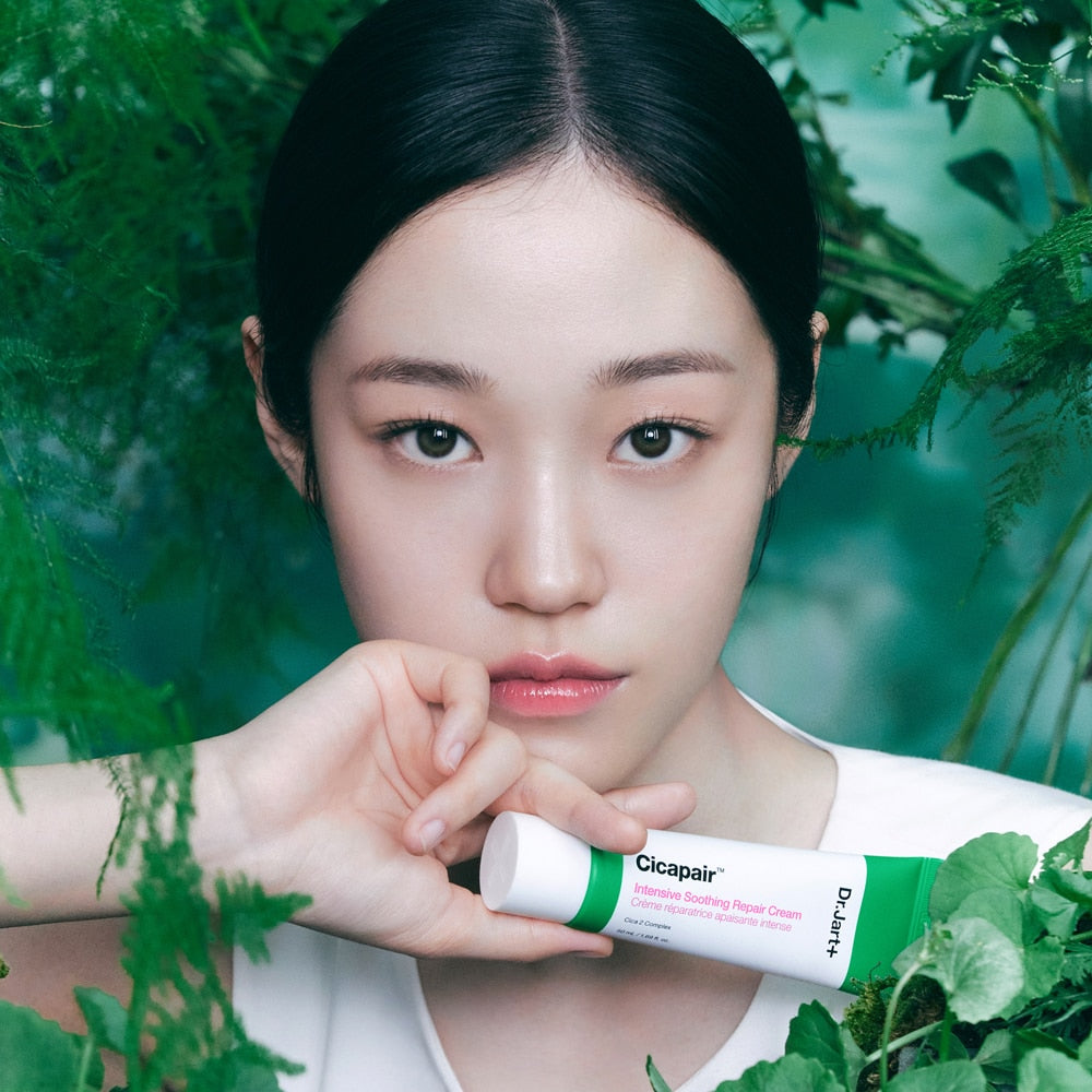 Person holding DR.JART+ Cicapair Intensive Soothing Repair Cream 50ml tube, surrounded by green foliage