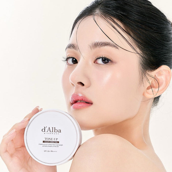 Close-up of a woman holding D'ALBA Vegan Tone-up Sun Cushion 15g 1 main product + 1 refill, showcasing radiant skin.