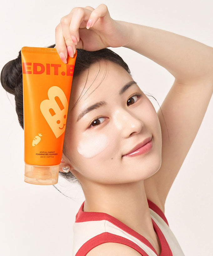 Woman holding EDIT.B Joyful Carrot Foaming Gel Cleanser 150ml next to her face, showcasing skincare application