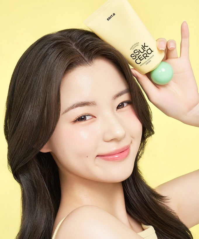 Smiling person holding EDIT.B Moisturizing Soothing Mugwort Ceramide Cream 100ml against a yellow background.