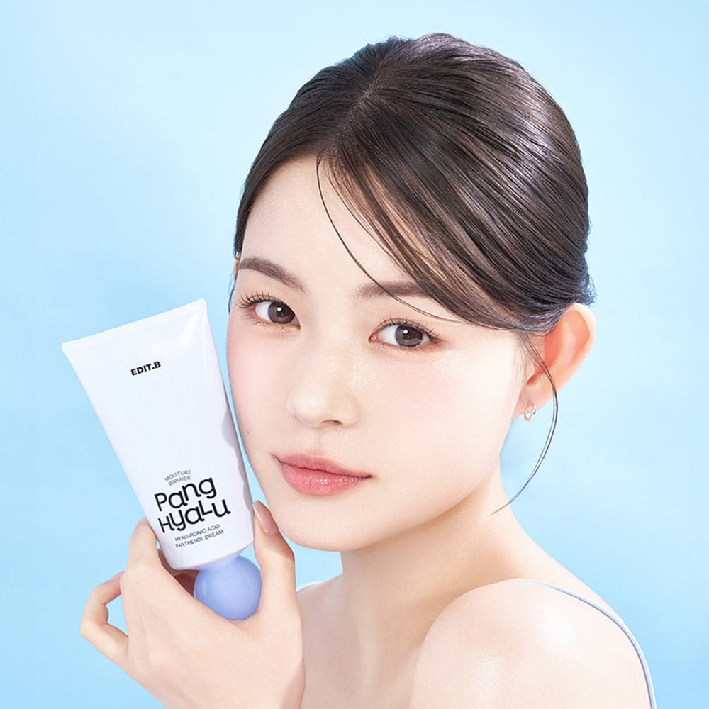 Woman holding EDIT.B Moisture Barrier Pang Hyaluronic Acid Pathenol Cream 100ml against blue background.