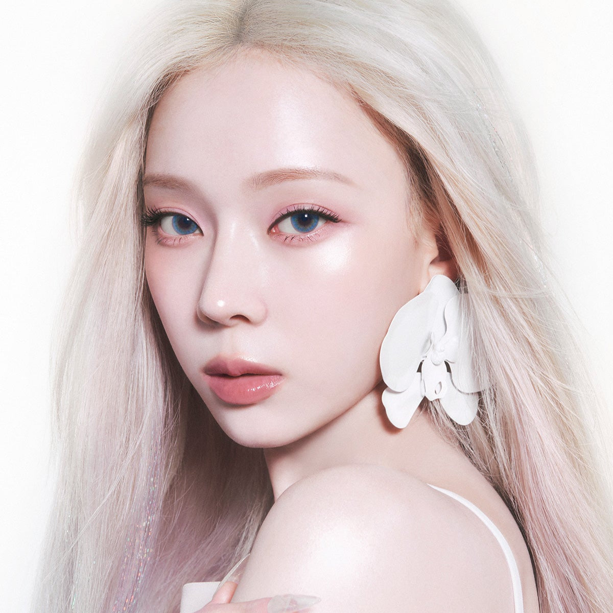 Portrait of a woman with platinum blonde hair and large white earrings, showcasing a glowing complexion.