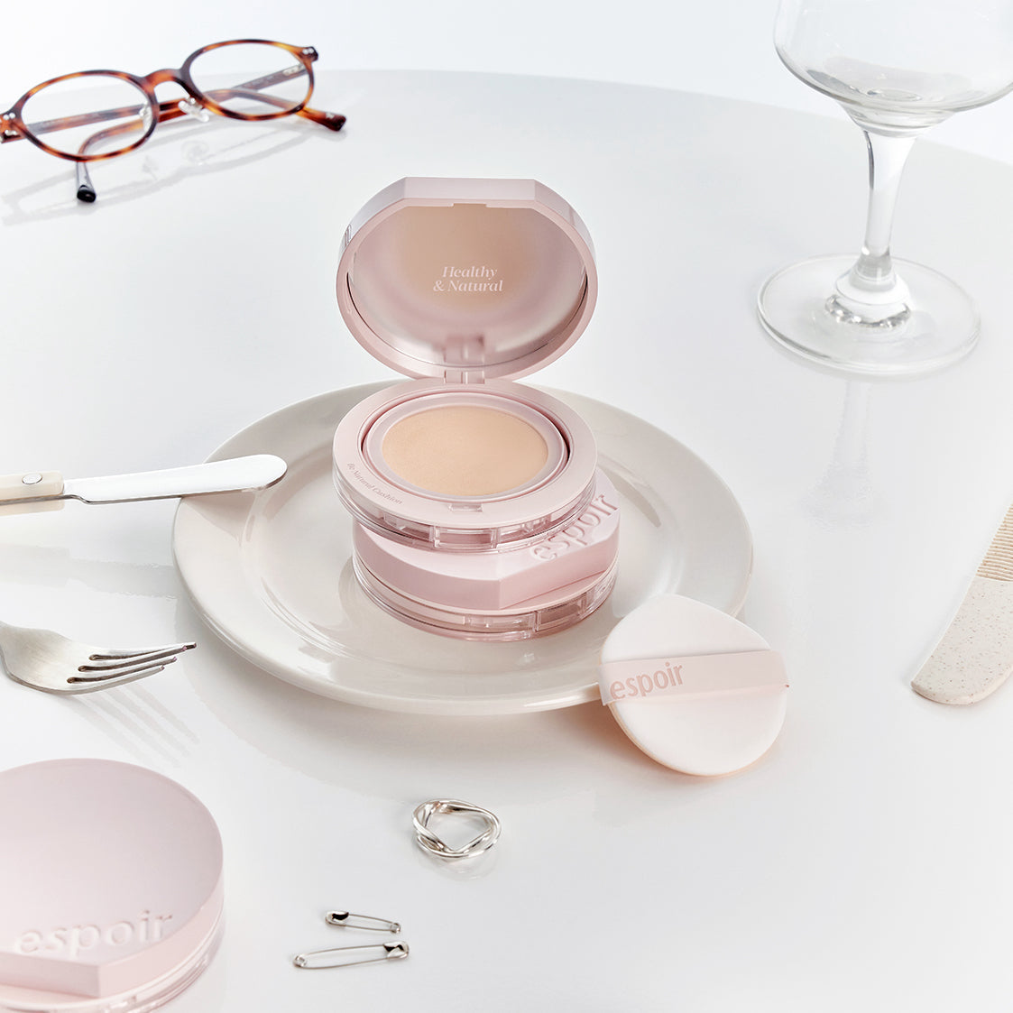 ESPOIR Be Natural Cushion SPF50+ PA++++ compact on a plate with accessories, highlighting its premium skincare and makeup benefits.