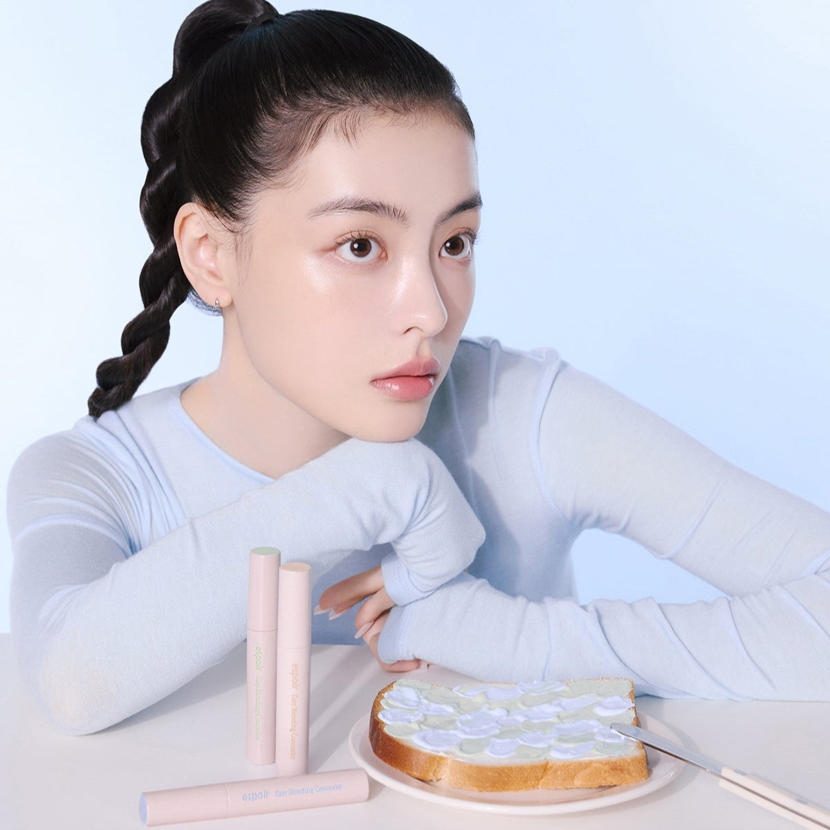 Model posing with ESPOIR EASY BLENDING CONCEALER next to toast on a plate, showcasing skincare and makeup product.