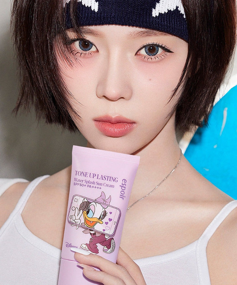 Person holding ESPOIR Water Splash Sunscreen Tone Up Lasting [Disney Edition] with cartoon character on packaging.