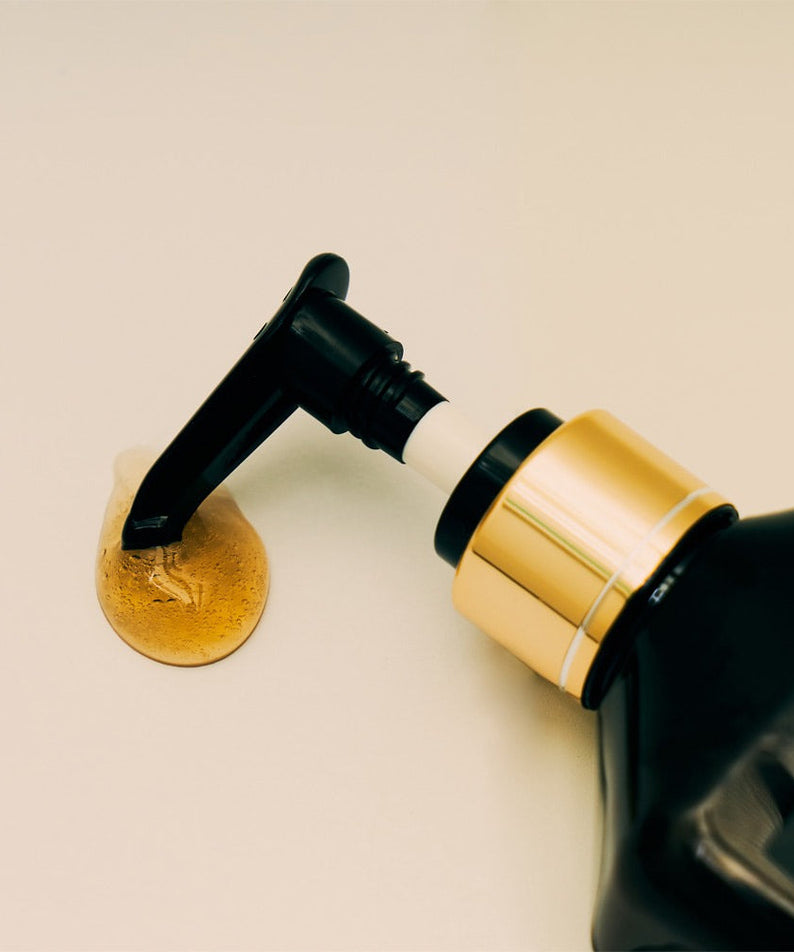 Close-up of QUA-T Samjin Out Oil 220ml bottle with pump dispenser and oil on a light surface.