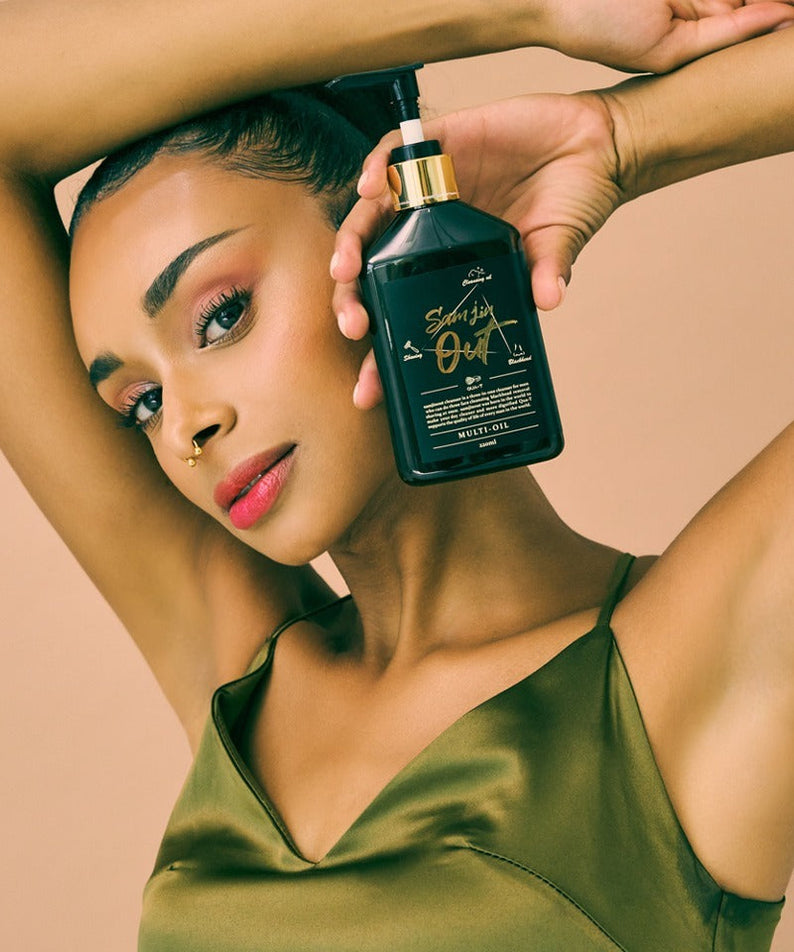 Woman holding QUA-T Samjin Out Oil 220ml against neutral background