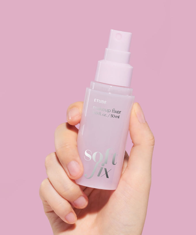 Hand holding ETUDE Soft Fix Makeup Fixer 50ml against pink background