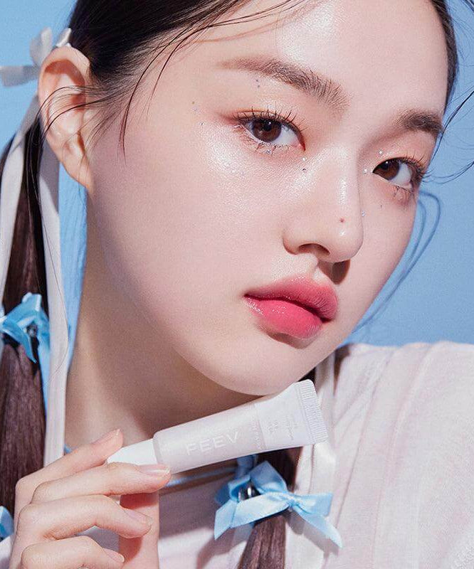 Woman holding a tube of FEEV Hyper-Fit Shimmering Serum with radiant skin and glossy lips