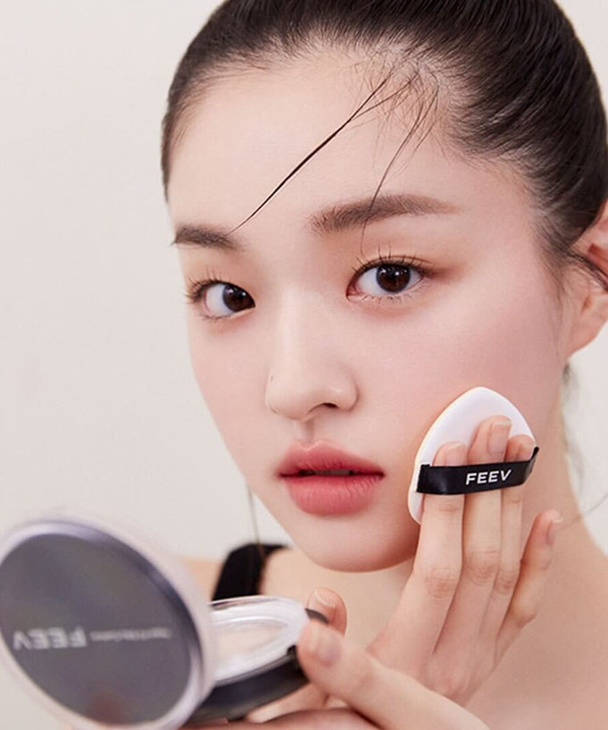 Woman applying FEEV Hyper-Fit Silky Cushion with makeup sponge for flawless coverage.