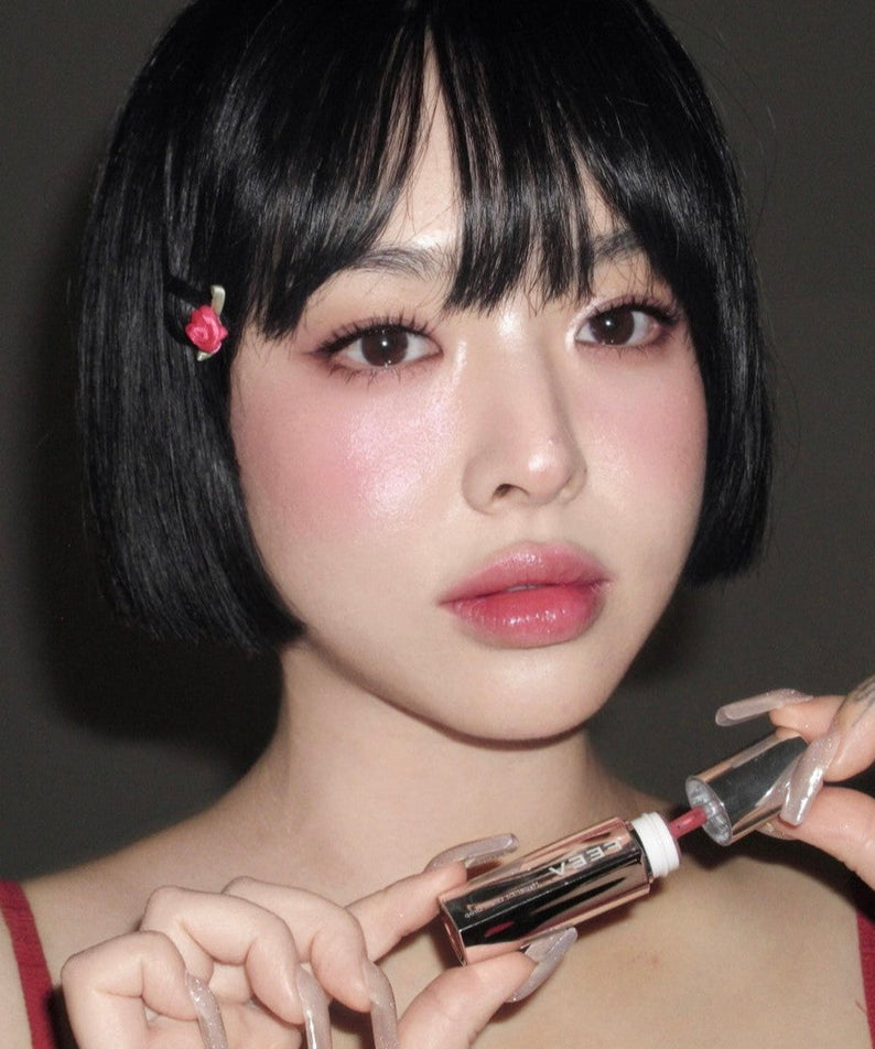 Portrait of a person holding FEEV Hyper-Fit Glam Drop with sleek bob hairstyle and floral clip, showcasing vibrant makeup look.