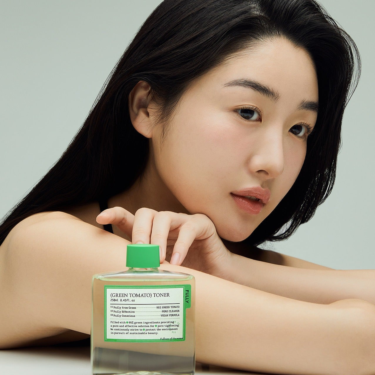 Woman holding a bottle of FULLY Green Tomato Toner 250ml, showcasing its packaging and design.