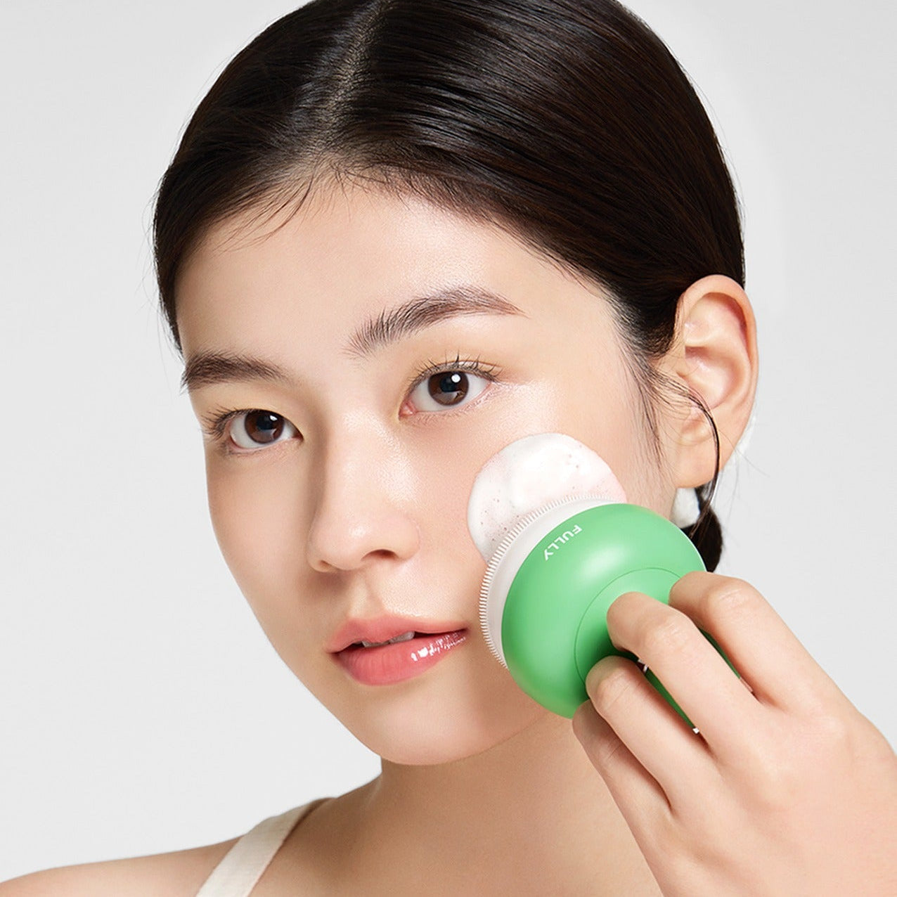 Woman using FULLY Pore brush with green handle for facial cleansing, showcasing skincare routine and effective pore care tool.