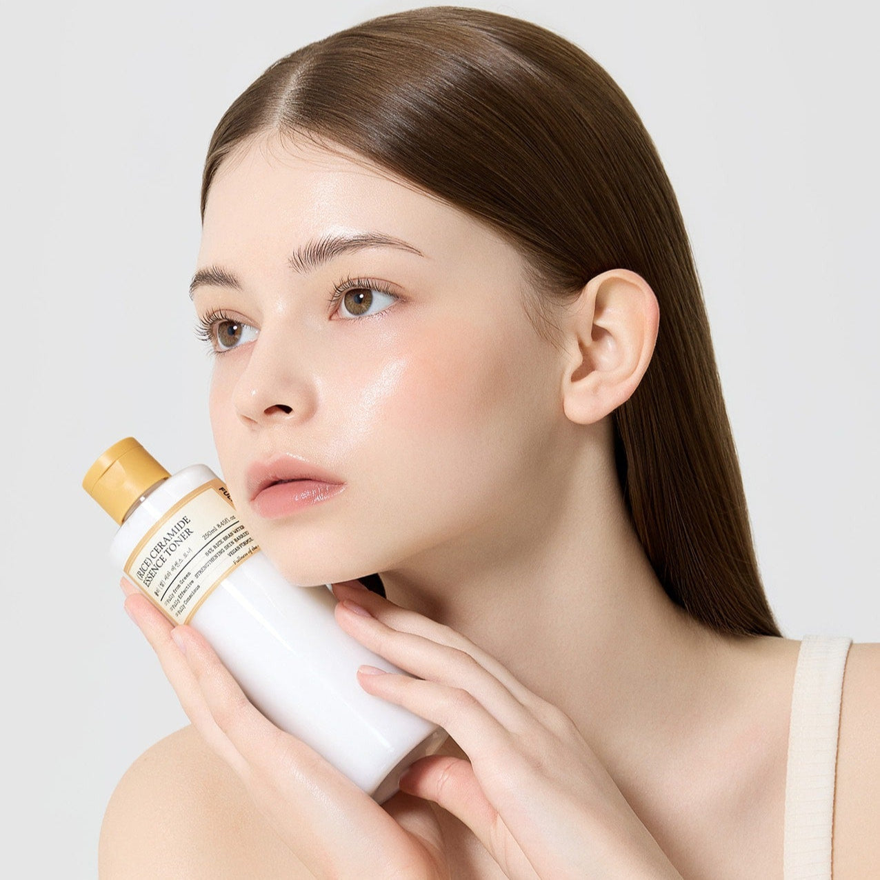 Model holding a bottle of FULLY Rice Serum Essence Toner 250ml with glowing skin.
