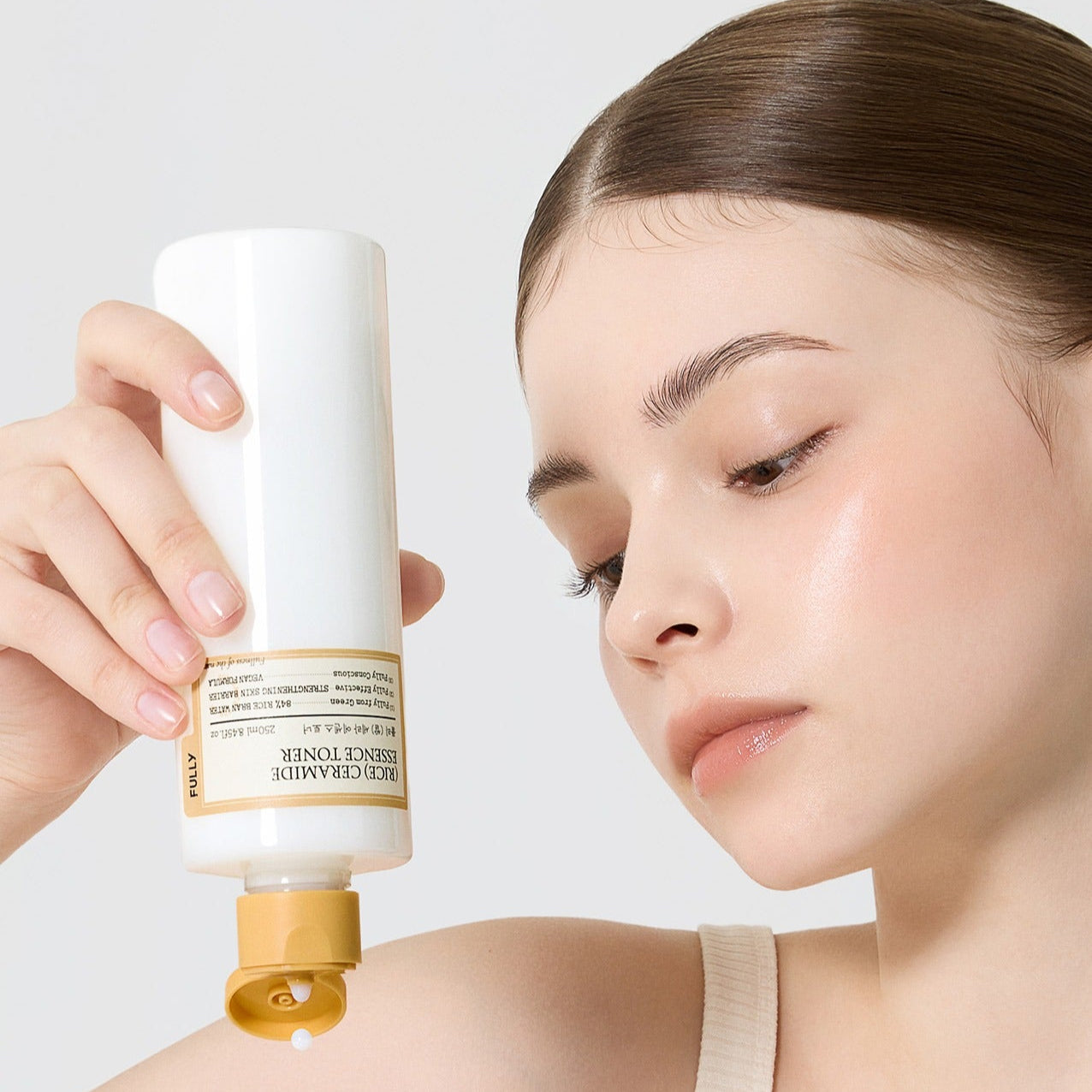 Woman using FULLY Rice Serum Essence Toner 250ml, holding the bottle to apply product to her skin