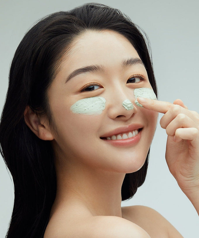 Woman applying FULLY Green Tomato Clay Pack Cleanser 120ml to her face, smiling, demonstrating skincare benefits.