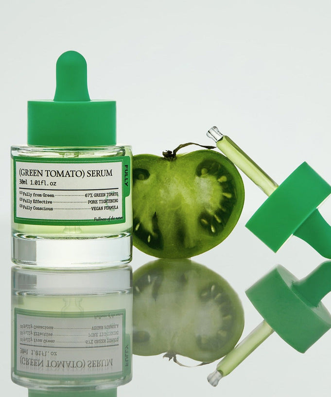 FULLY Green Tomato Serum 30ml with a sliced green tomato and dropper on a reflective surface showcasing skincare serum.
