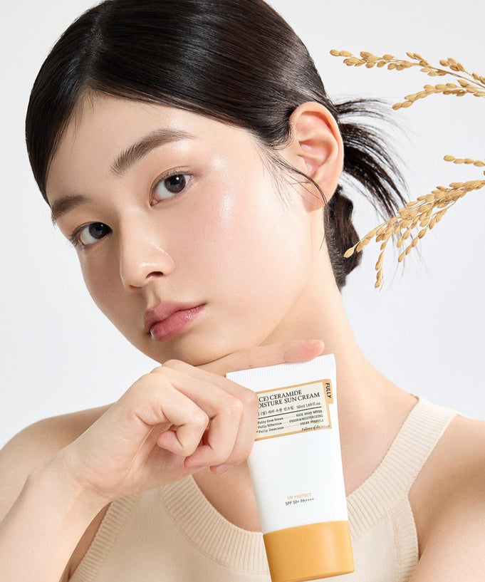 Woman holding FULLY Rice Sera Moisture Sunscreen 50ml with rice plant in the background