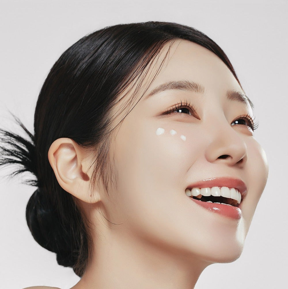 Smiling woman applying skincare, showcasing the brightening effect of GENABELLE PDRN Enriched Recovery Balm 50ml on radiant skin.