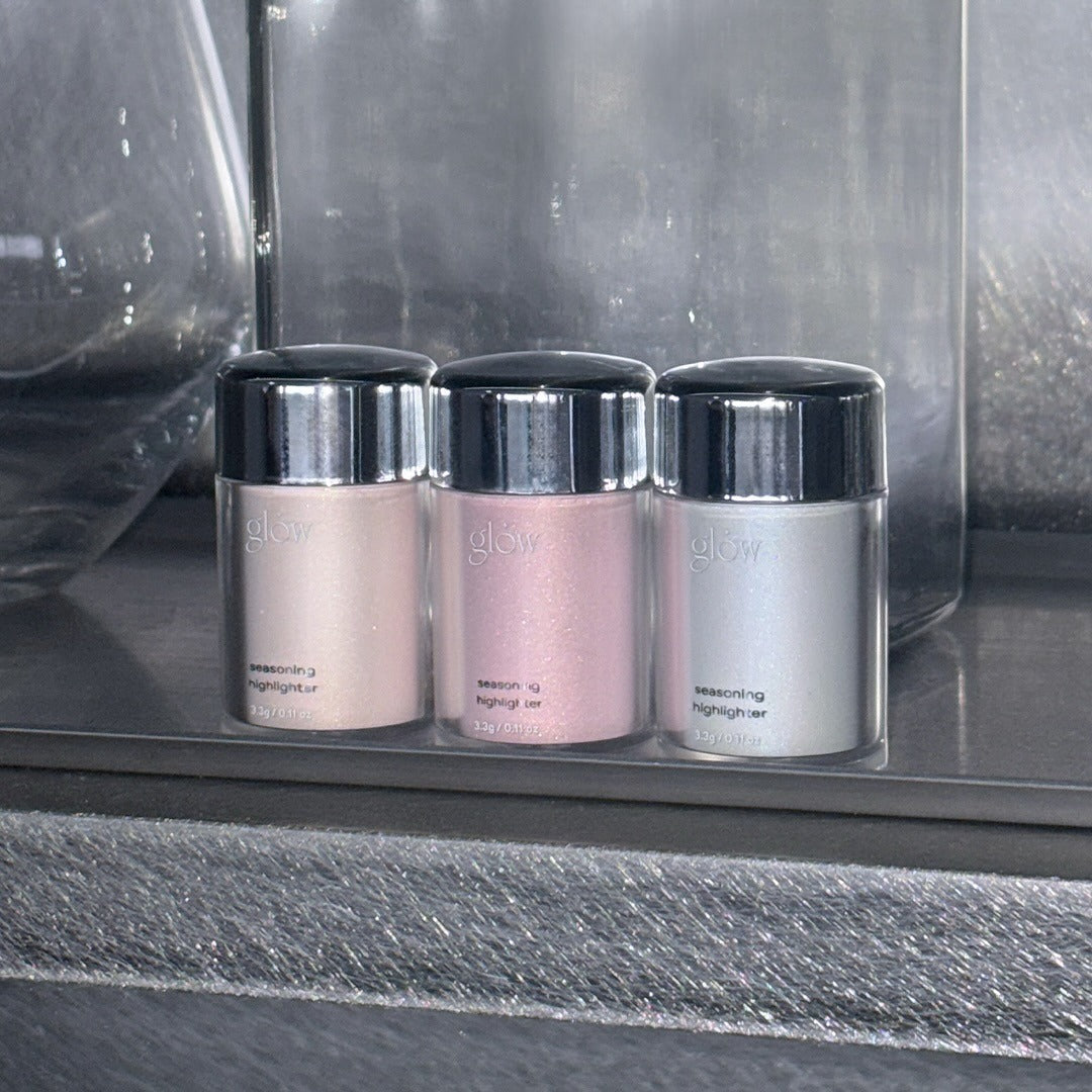 Three GLOW Seasoning Highlighter bottles in pink, silver, and beige shades on display.