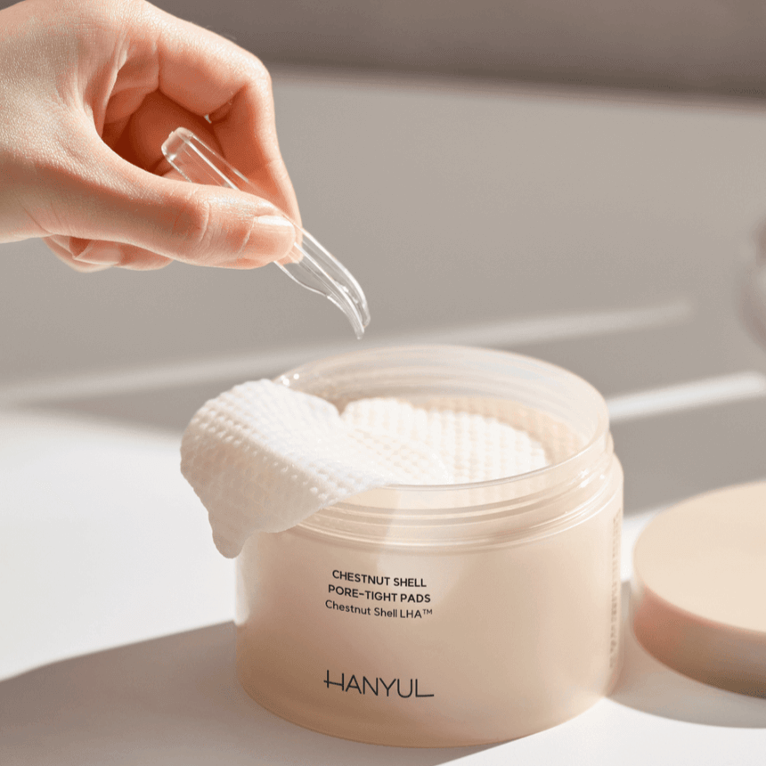Hand using tweezers to pick up a pad from HANYUL Buddleberry Pore Tightening Pad jar on a white background.