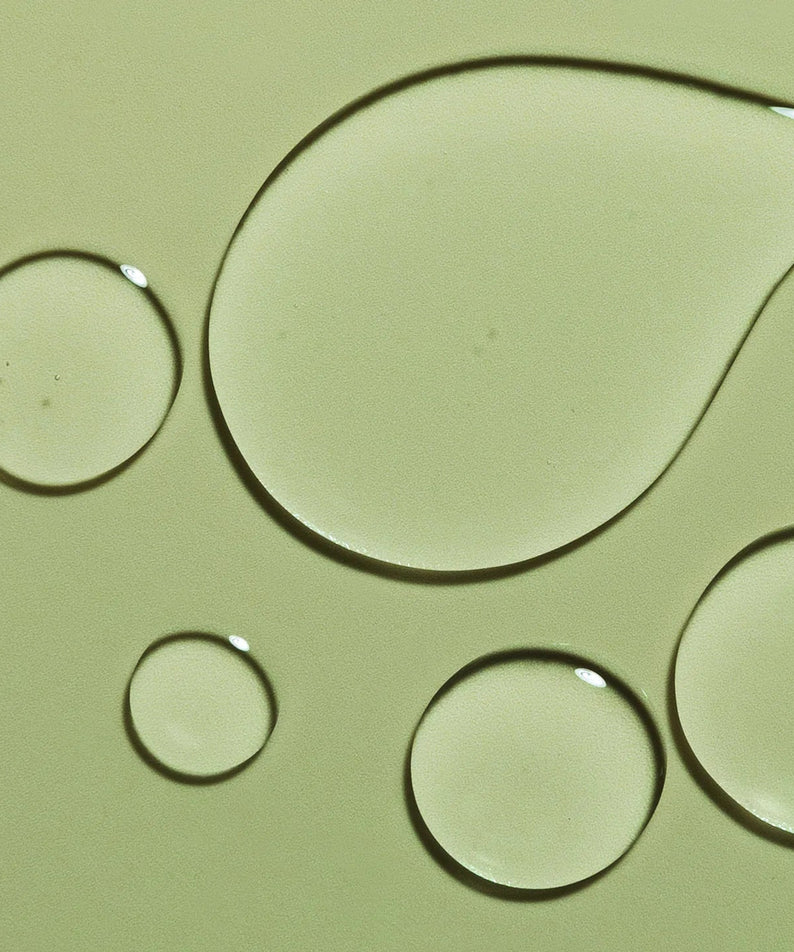 Droplets of HARU HARU Black Rice Hyaluronic Toner Unscented 150ml on a green background.