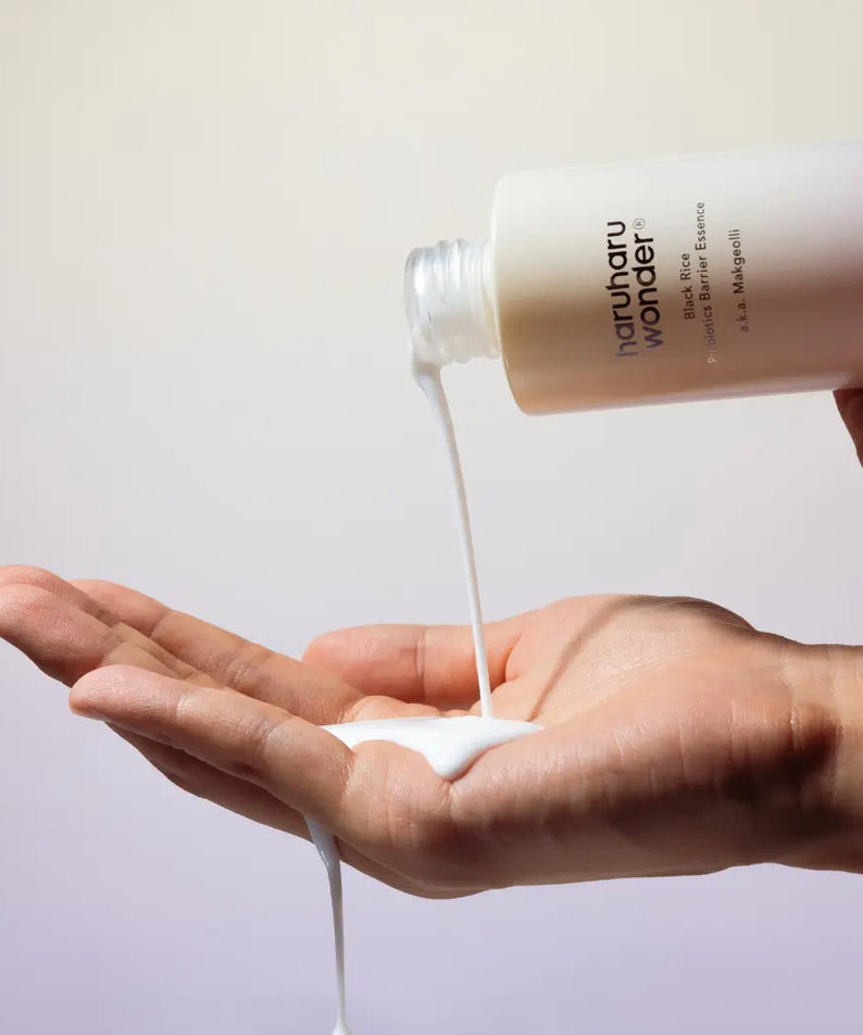 HARUHARU Black Rice Probiotics Barrier Essence 120ml being poured onto a hand, showcasing the product's texture and application.