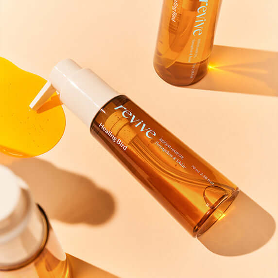 HEALING BIRD Revive Repair Hair Oil 70ml bottle on a light surface with a splash of oil nearby.