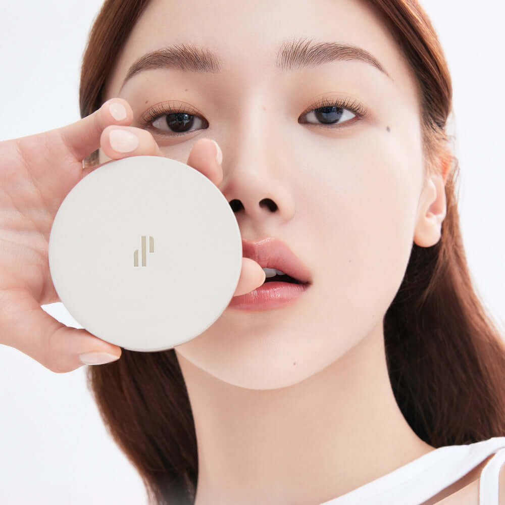 Model holding HEART PERCENT Dot ON Mood Layer Cushion compact in front of face, featuring minimalist design and elegant packaging.