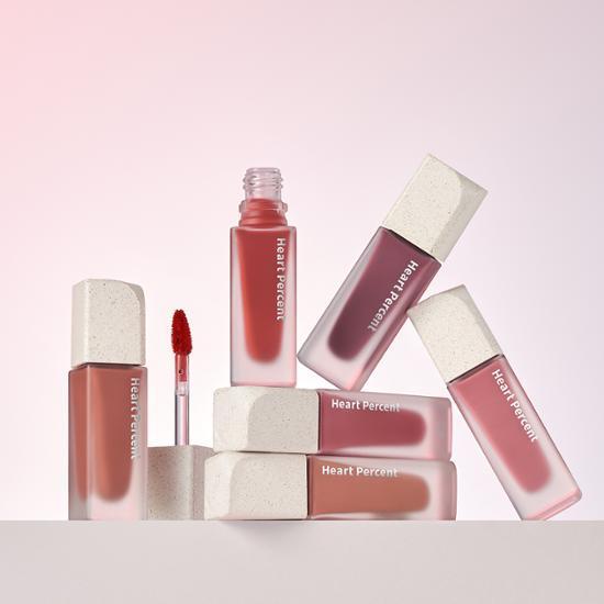 HEART PERCENT Dote On Mood Blurry Fog Tint lip products arranged in a creative display on a pink background.