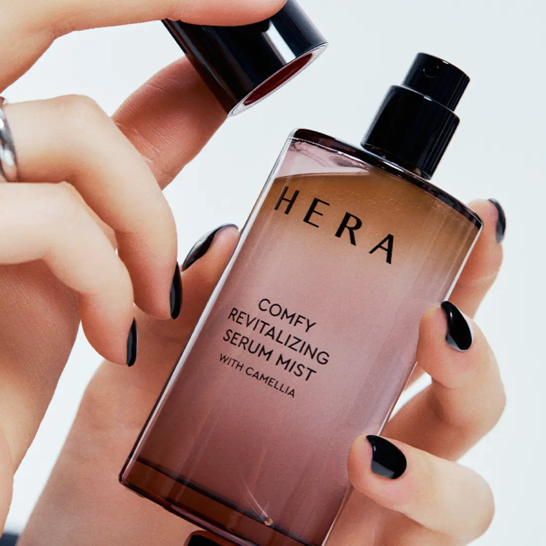 HERA Comfy Revitalizing Serum Mist 90ml bottle being held, highlighting the product's sleek design and luxurious appearance.