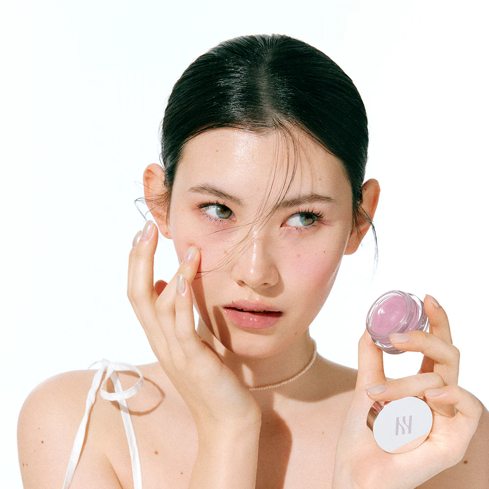 Woman applying HERA Sensual Lip & Cheek 7g to her cheeks, showcasing versatile makeup use.